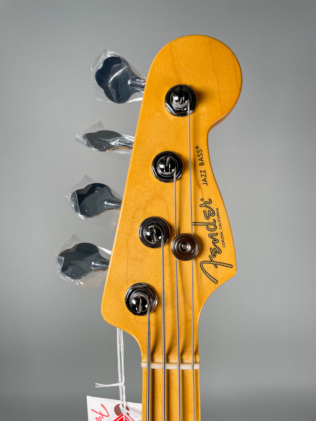 Close-up of the light-colored headstock, angled slightly left, showing four chrome tuning pegs, three still in plastic wrap.