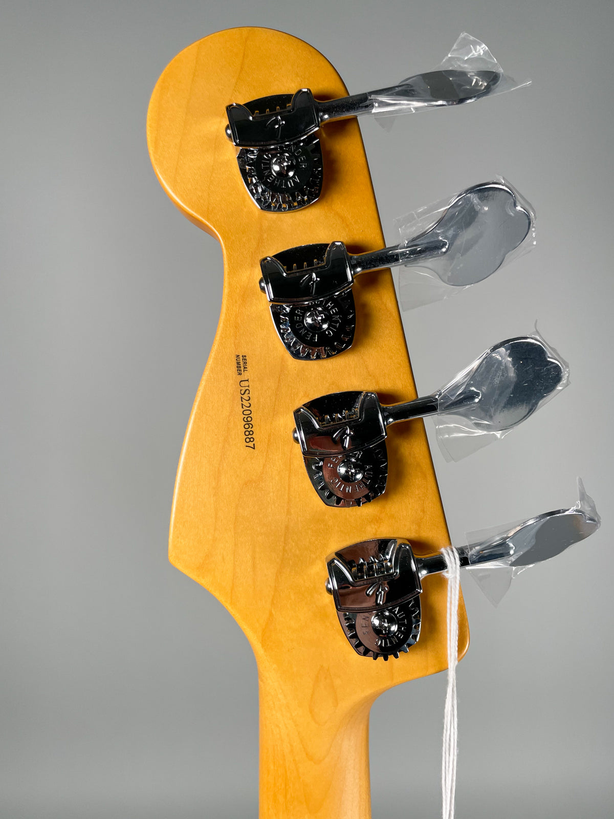 The back of a light maple headstock and neck, with four chrome tuners, their paddles still in plastic wrap.