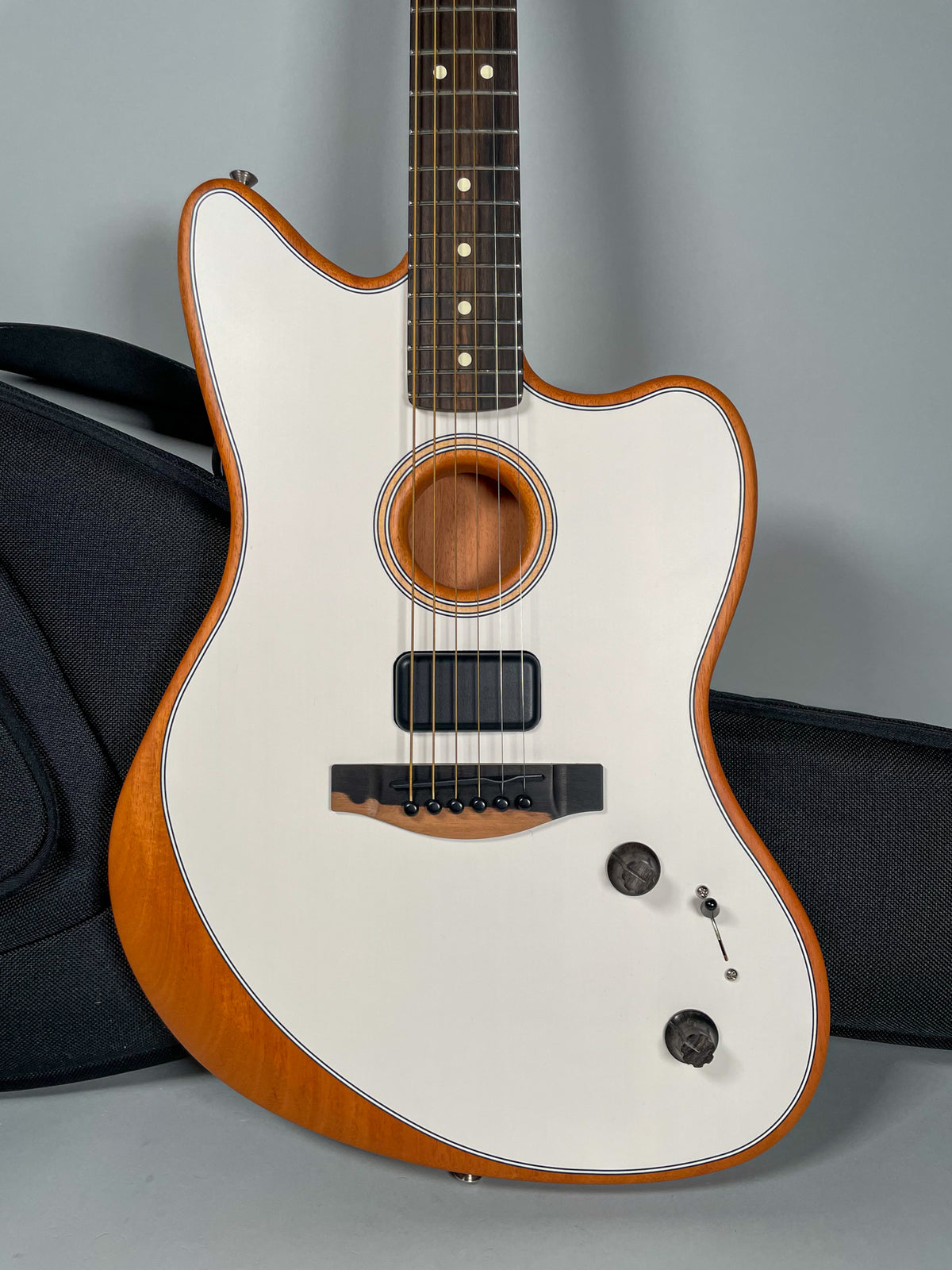Full-body view of a white Jazzmaster-style acoustic guitar with a natural wood back and sides, black bridge, and two black control knobs.