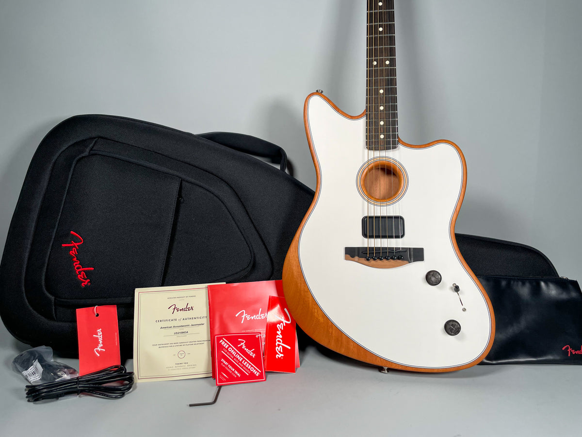 White Jazzmaster-style guitar with a natural wood body edge, black bridge, two black control knobs, and a black gig bag.