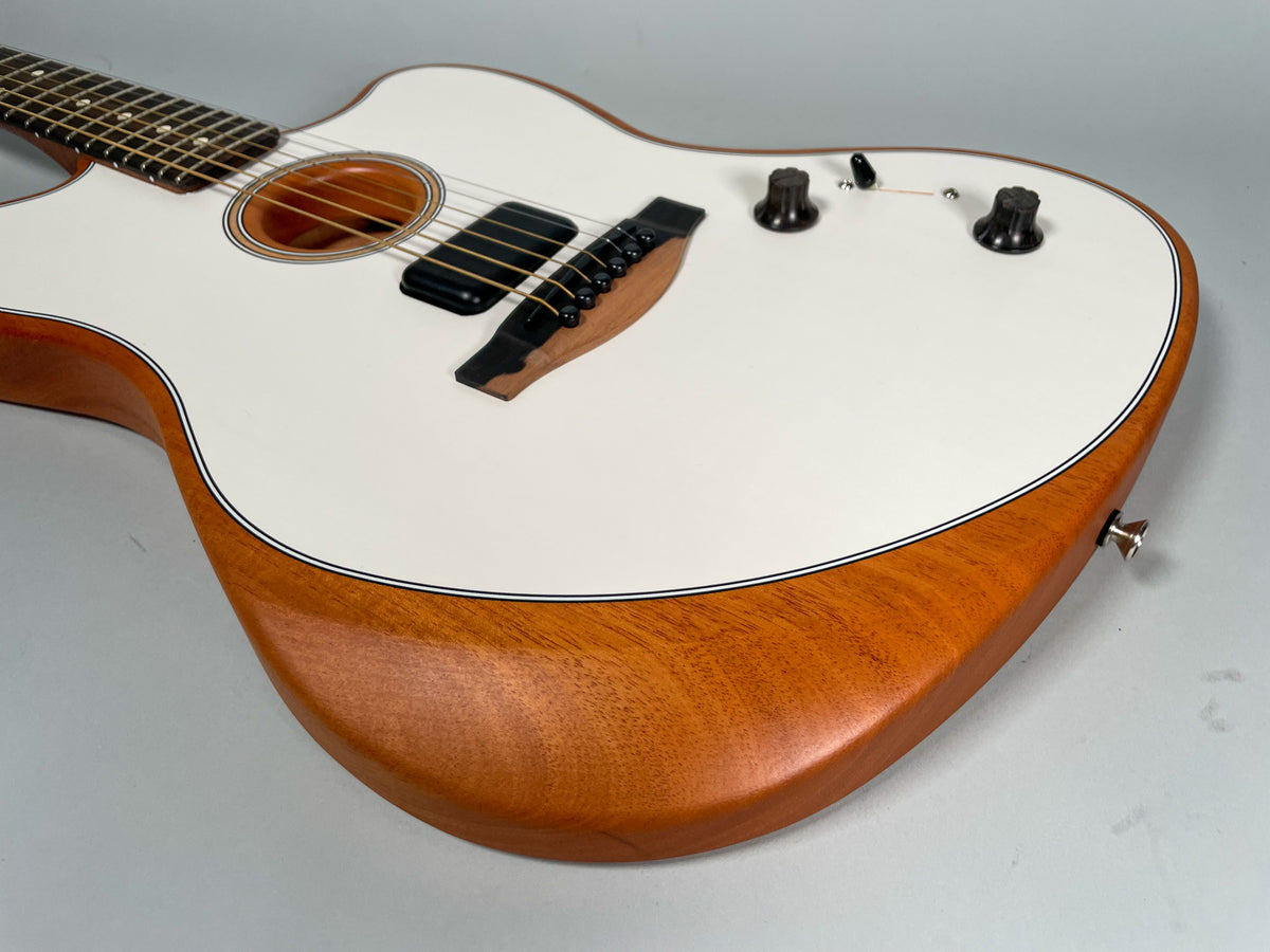 The white-topped guitar, angled from the neck, shows its natural wood sides, soundhole, black pickup, bridge, and three control knobs.