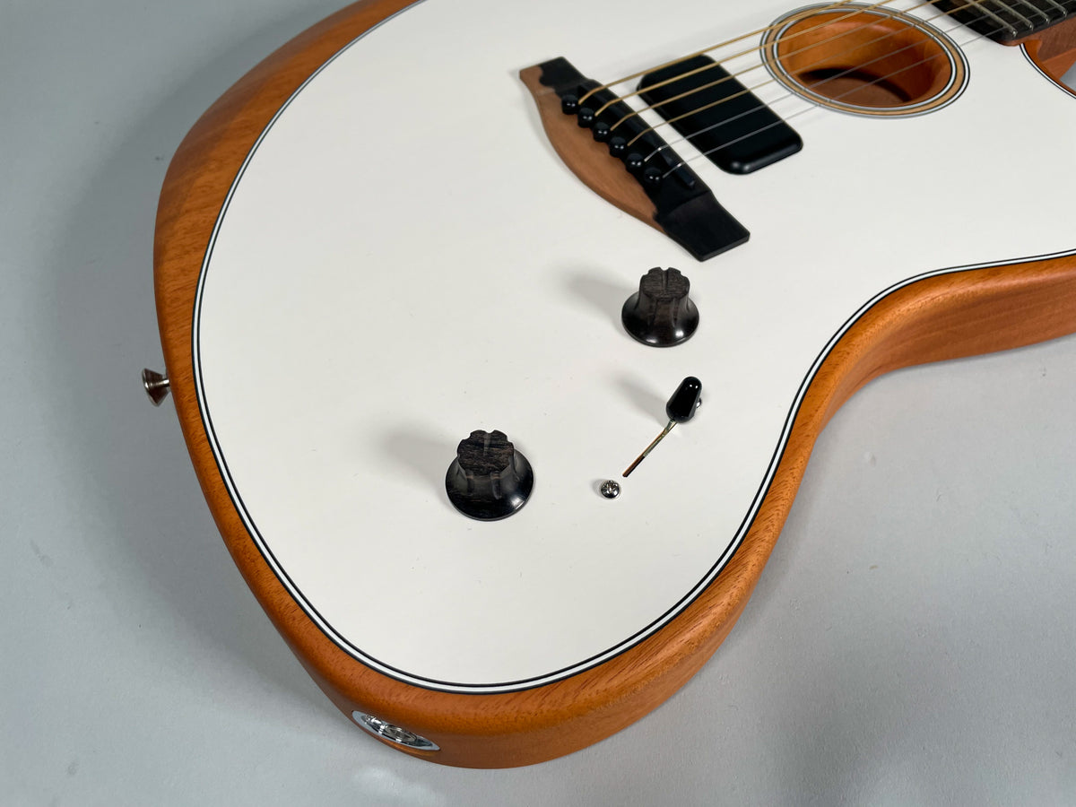 Close-up of the guitar's lower body, showing the white top, natural wood sides, two black control knobs, and a black pickup selector switch.