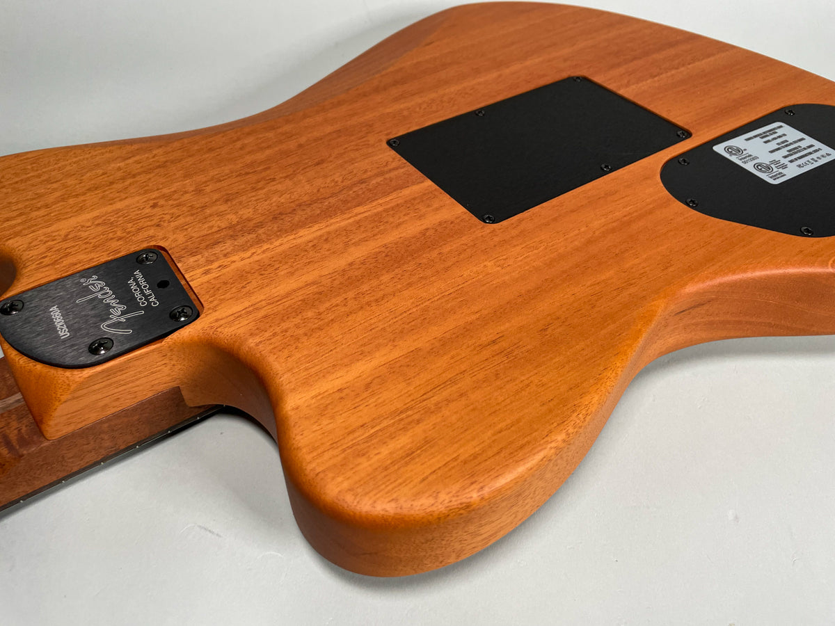 Angled view of the guitar's back, showing the light brown wood grain, two black control plates, and the neck joint.