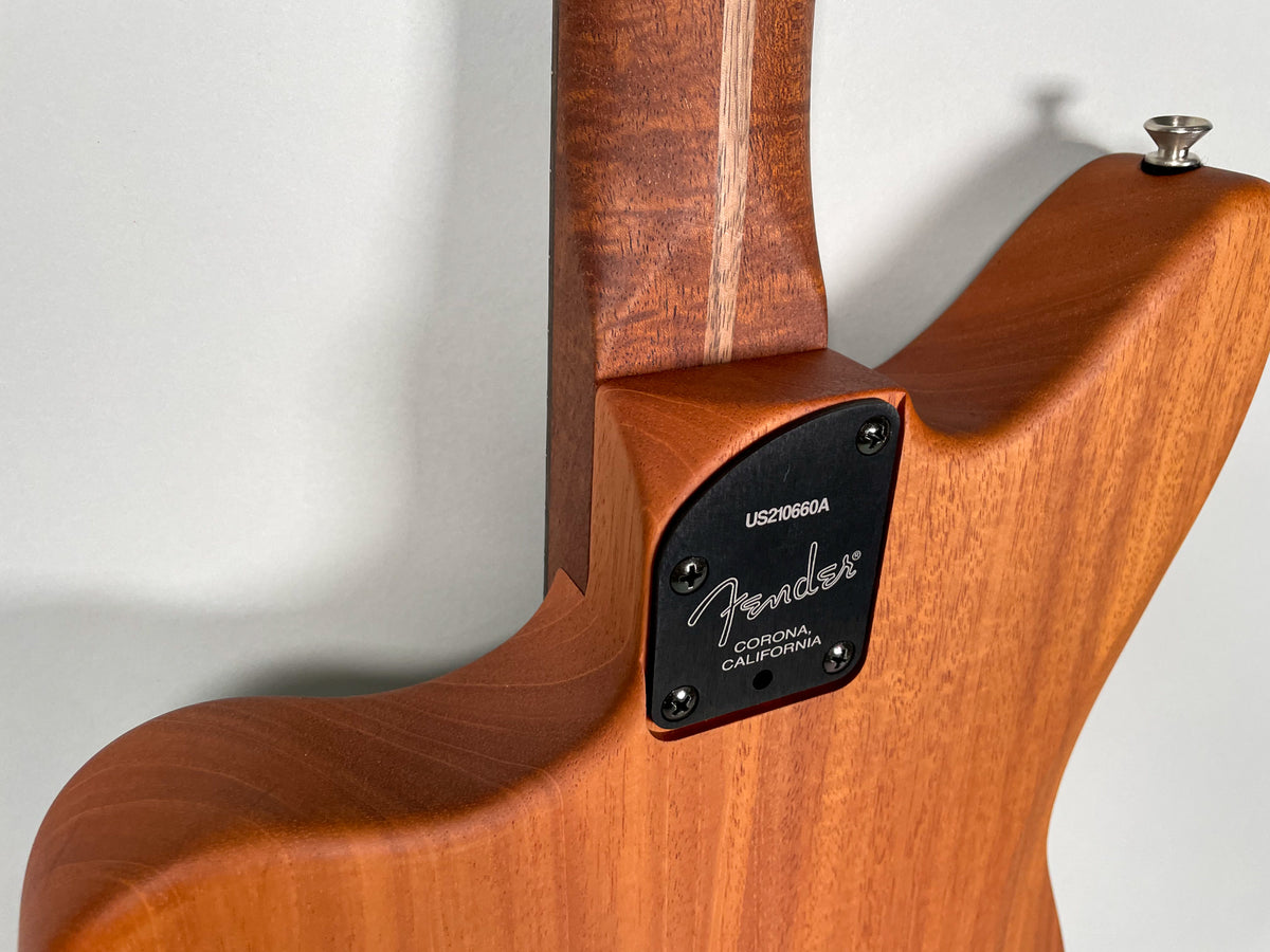 Close-up of the guitar's natural wood back, showing the neck joint and a black metal plate with "Fender Corona, California" engraved.
