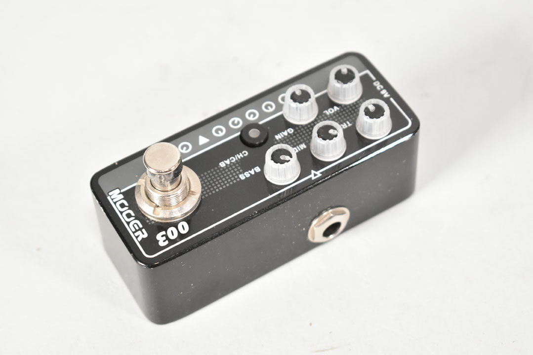 Black mini pedal with a silver footswitch, six clear plastic knobs, a small black button, and a visible input jack on the right side.