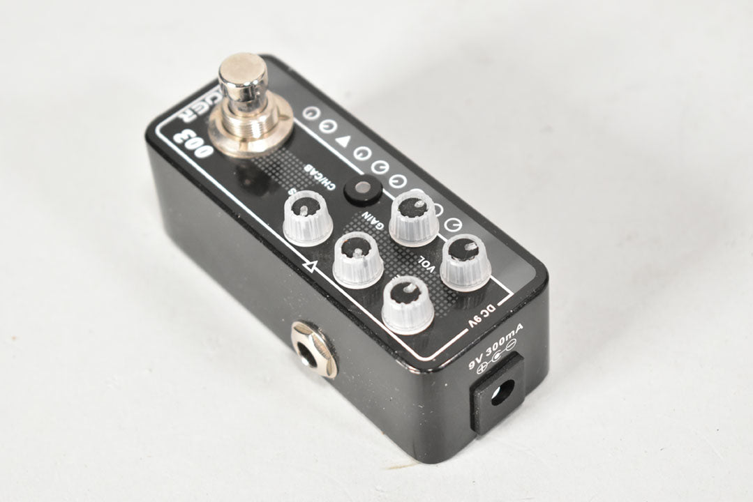 Black mini pedal with a chrome footswitch, five clear control knobs, a black button, and input/power jacks visible on the sides.