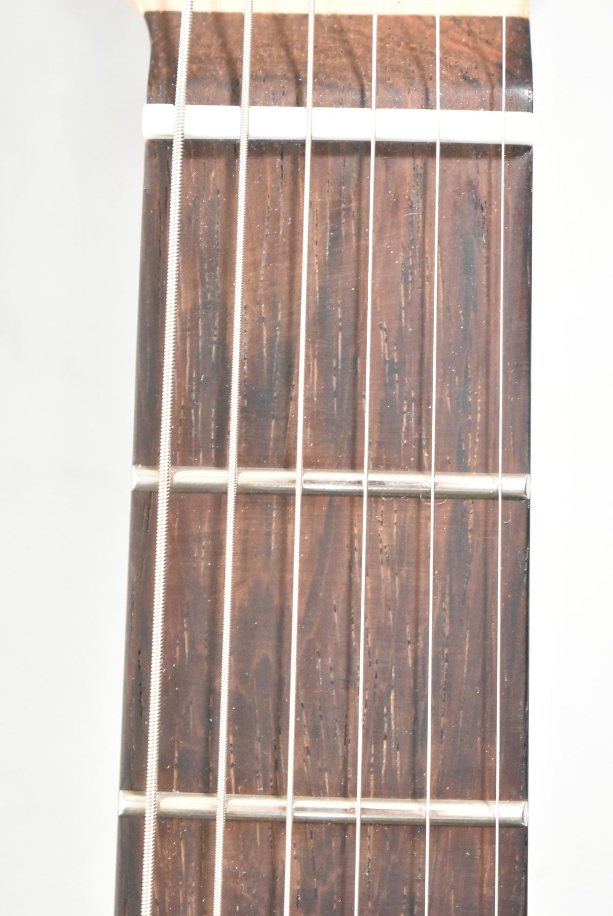 Close-up of the dark brown fretboard with silver frets and six strings, showing light wear and dust on the wood.