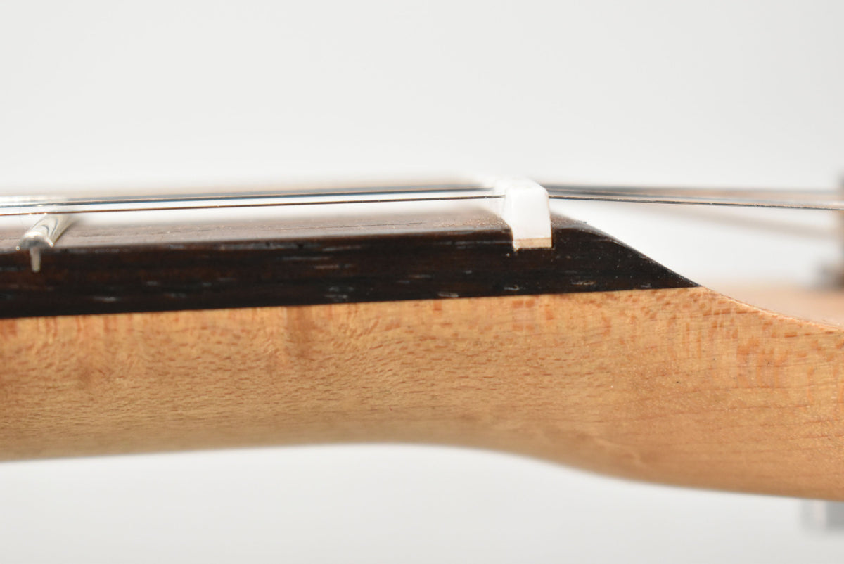 Close-up of the guitar's neck, showing the dark fretboard, white nut, and light wood grain of the neck, with strings visible.