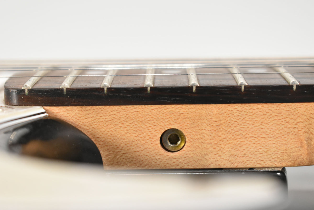 Close-up of the guitar neck heel and lower fretboard, showing a dark rosewood fretboard, light maple neck, and a truss rod access hole.