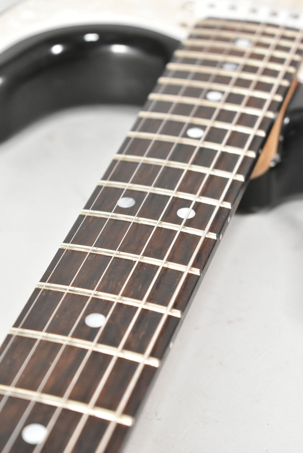 Close-up of the dark rosewood fretboard with white dot inlays, showing light wear on the frets and a glimpse of the sunburst body.