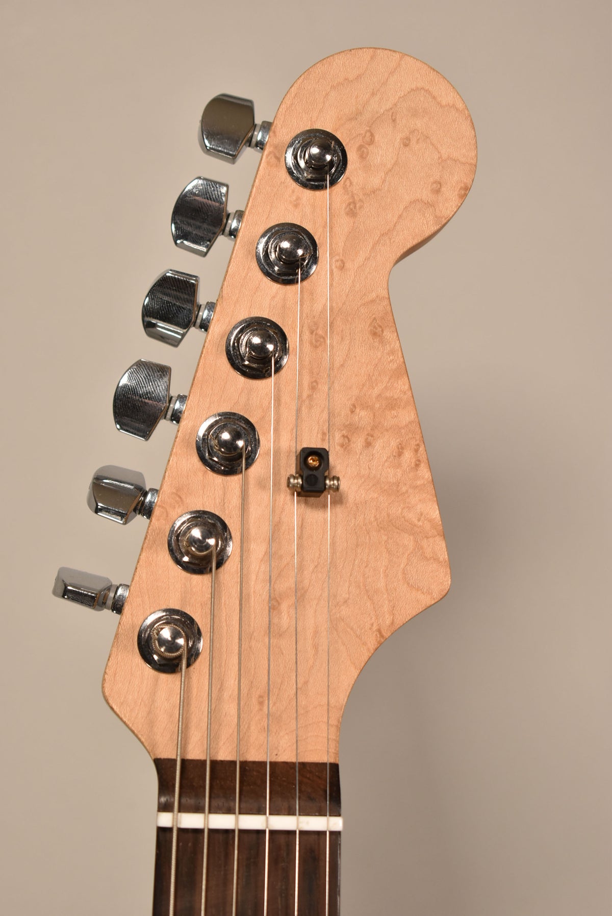 The guitar's headstock, angled slightly right, is light wood with a subtle burl pattern, six chrome tuners, and a string tree.