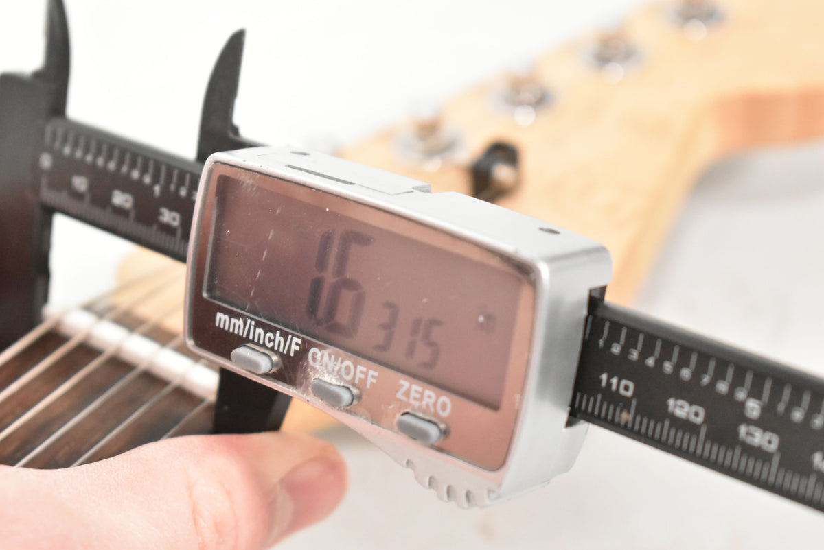 A digital caliper measures the guitar's nut width at 1.6315 inches, with a maple neck and dark fretboard visible.