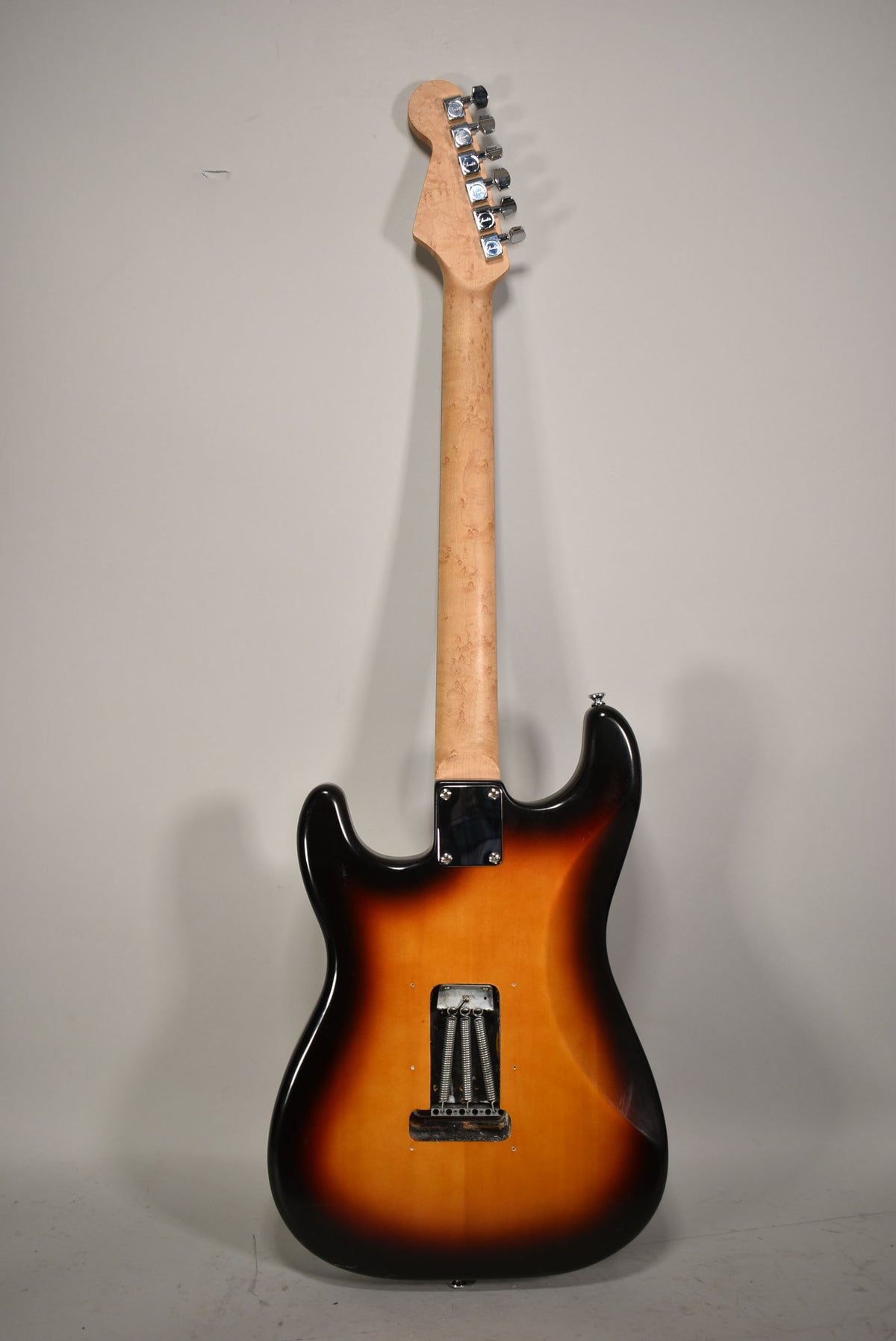 The guitar's back shows a sunburst finish, a maple neck with a figured grain, and the tremolo spring cavity with three springs.