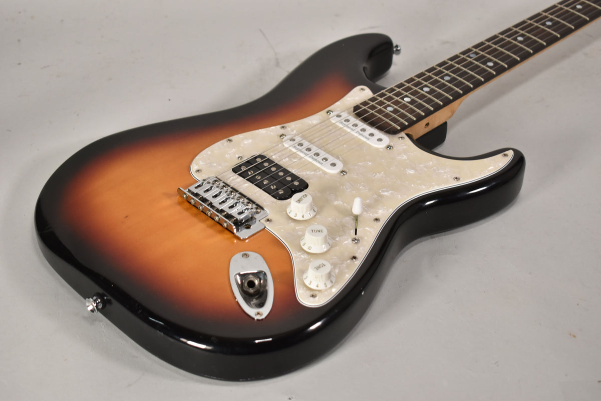The sunburst Strat-type guitar, angled from the lower bout, shows a pearloid pickguard, HSS pickups, and three white control knobs.