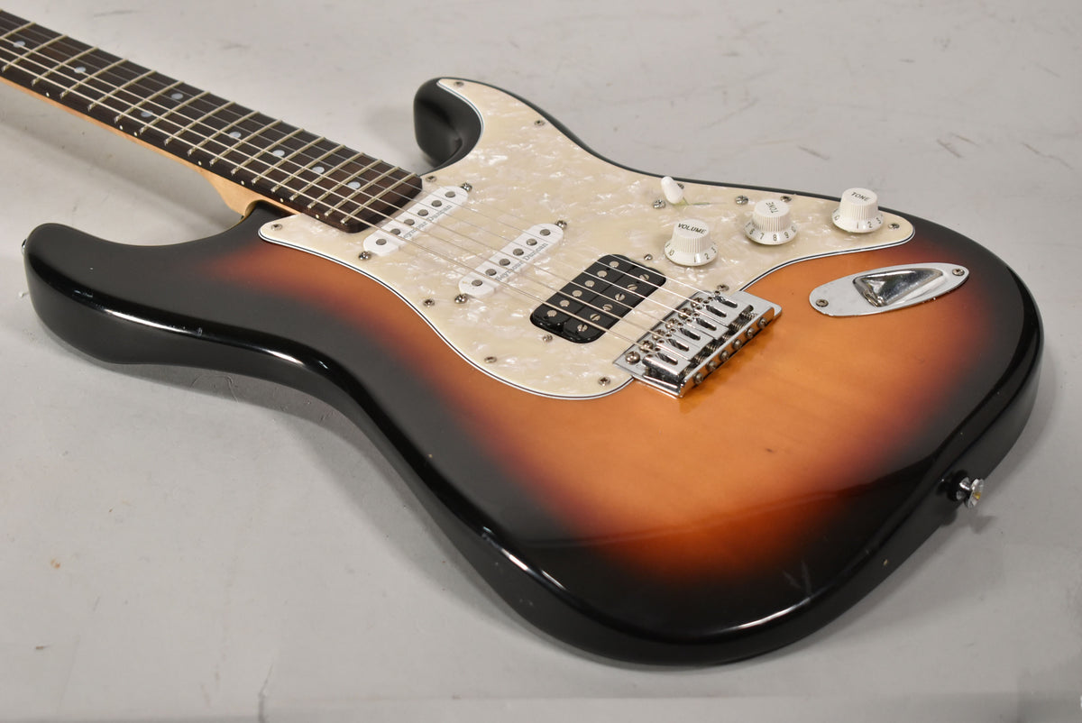The sunburst Strat-type guitar is angled from the neck, showing its pearloid pickguard, chrome hardware, and white control knobs.