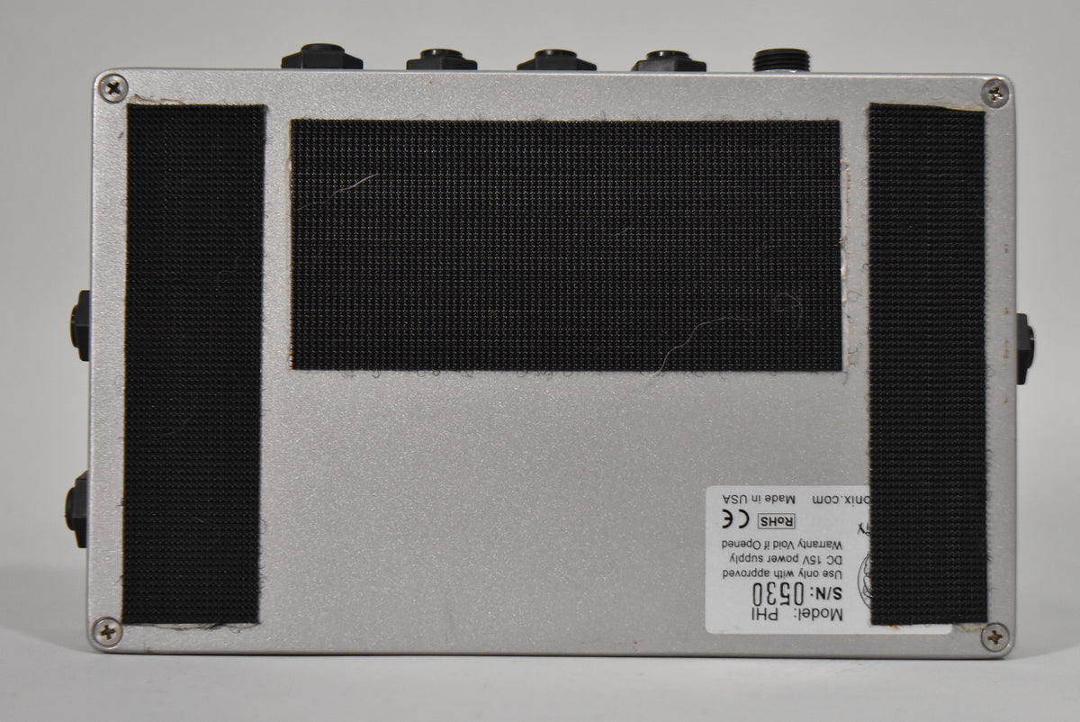 The pedal's silver-grey bottom is shown, covered by three black textured grip pads and a white serial number sticker.