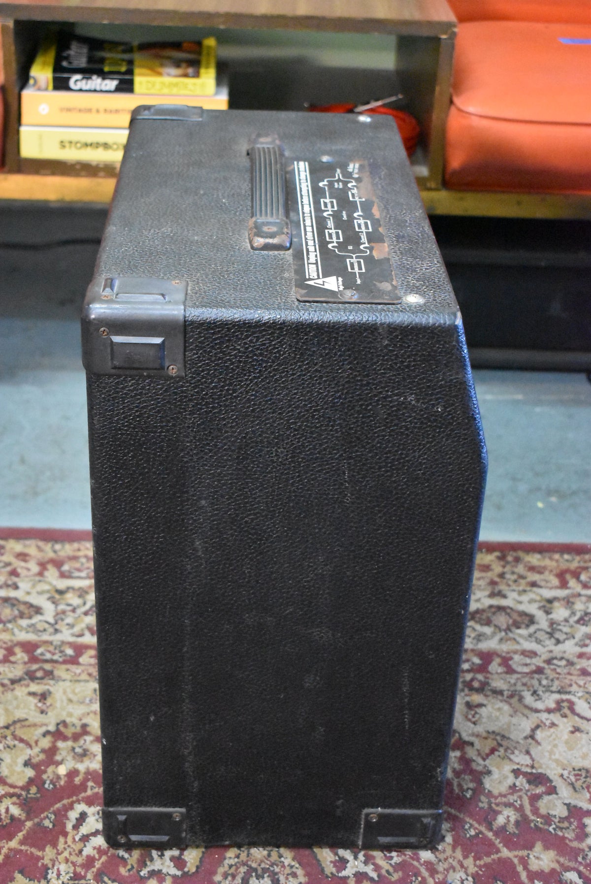 The black textured combo amp is viewed from the top right, showing the top handle, metal corner protectors, and a worn diagram.