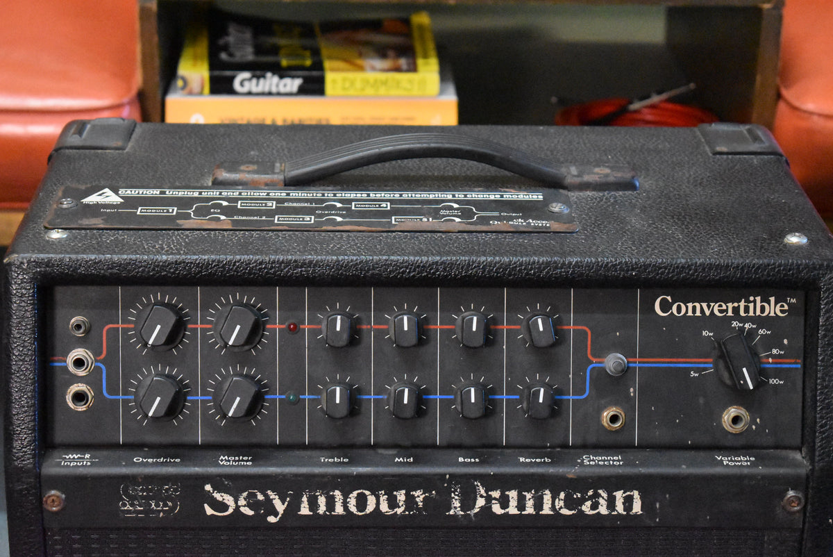 The black textured combo amp is viewed from above, showing its top handle and a busy front panel with 14 black knobs.