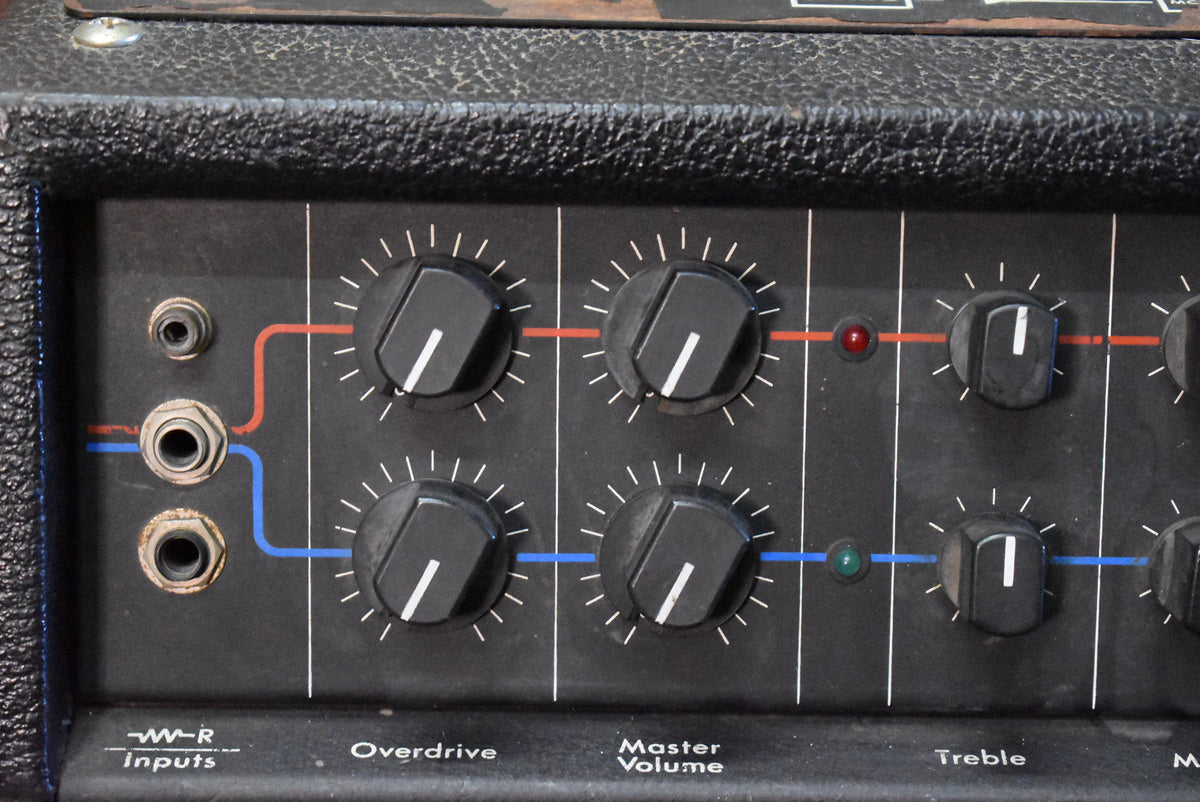 Close-up of the amp's black control panel, showing three input jacks, eight black knobs with white indicators, and red and green LEDs.