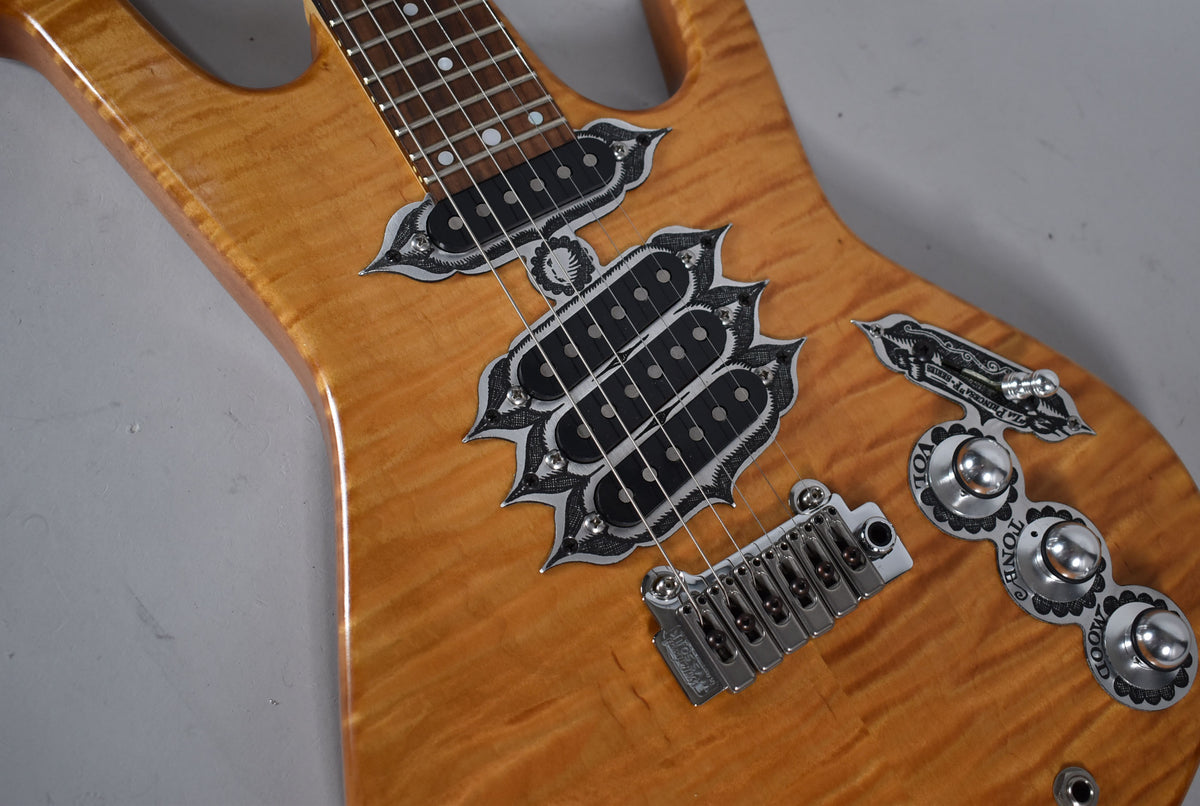 Close-up of the guitar's natural flame maple body, showing ornate metal pickup surrounds, a chrome bridge, and three dome-top control knobs.