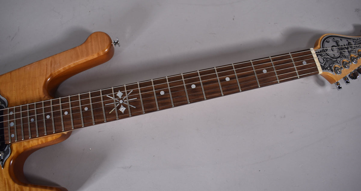 Close-up of the natural finish guitar's neck and headstock, showing snowflake fretboard inlays and engraved metal headstock overlay.