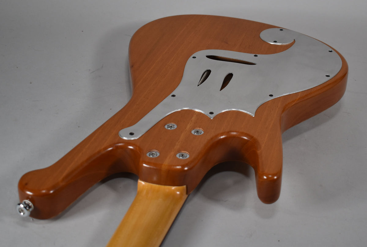 The guitar's natural wood back, with a light brown finish, features a large, ornate brushed aluminum backplate.