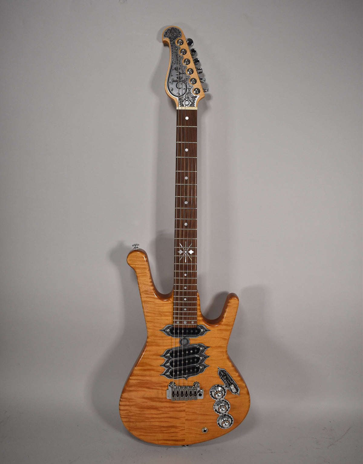Full-front view of a natural finish electric guitar with a flame maple top, ornate metal hardware, and a decorated headstock.