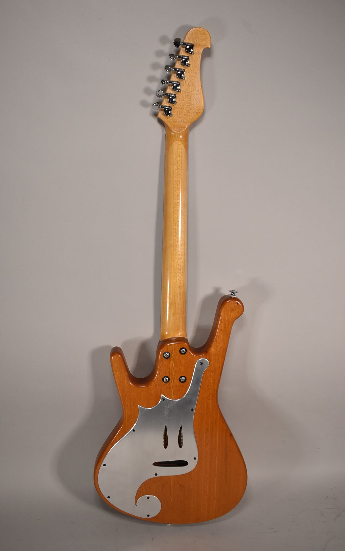 The guitar's natural wood back, neck, and headstock are visible, with a brushed metal control plate and chrome tuners.