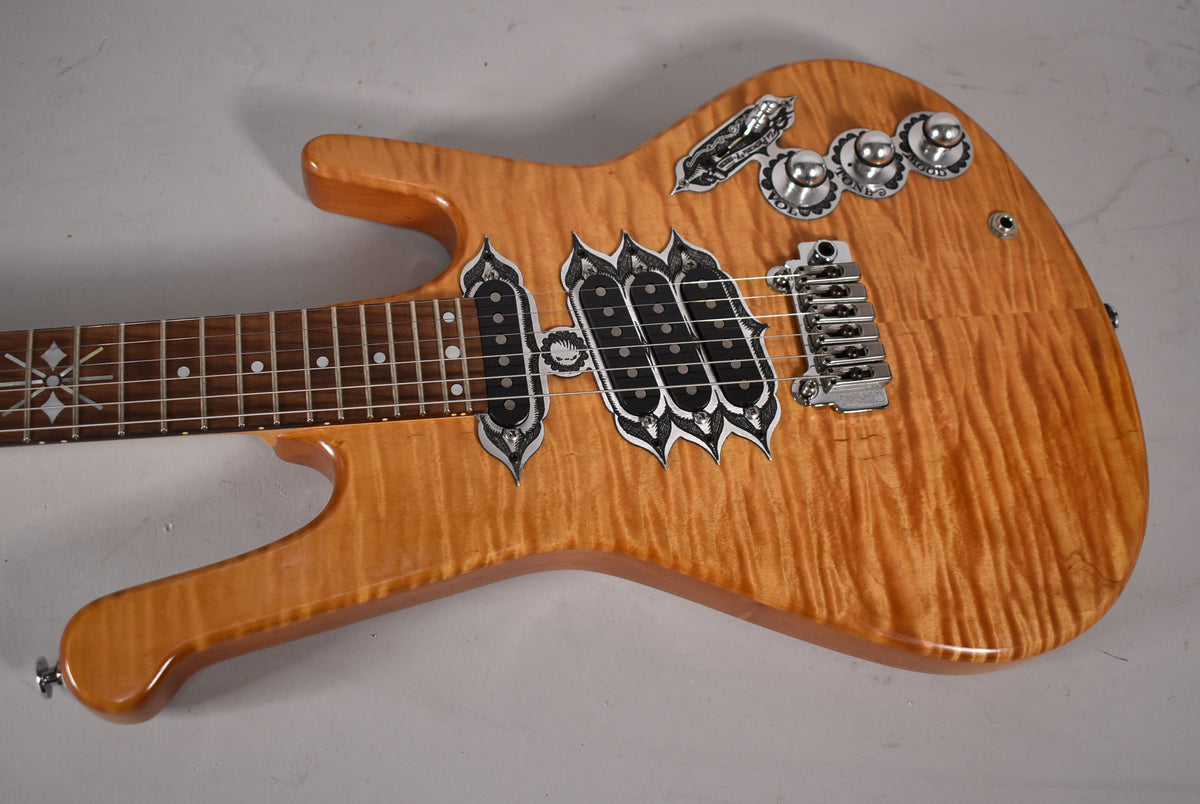 Close-up of the natural flame maple body, showing ornate silver pickup surrounds, three control knobs, and a chrome bridge.