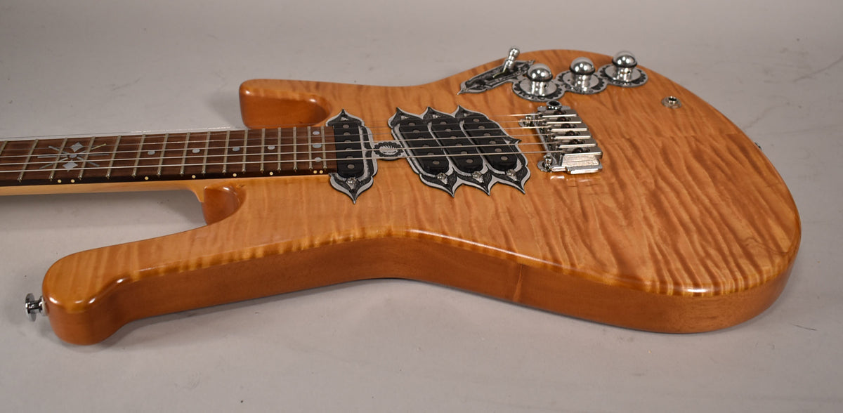 The natural finish electric guitar body, with a flame maple top, is angled from the neck to the lower bout, showing ornate black pickups and chrome hardware.