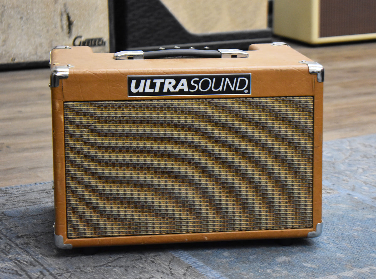 Front view of a tan combo amp with a black handle, chrome corner protectors, and a brown and gold grille cloth.