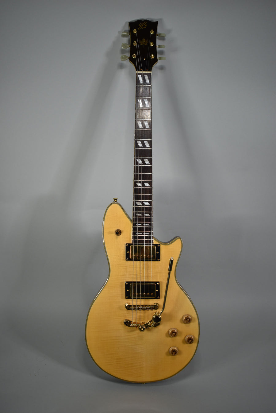 Full-length view of a natural finish electric guitar with a flame maple top, gold hardware, two humbuckers, and a vibrato tailpiece.