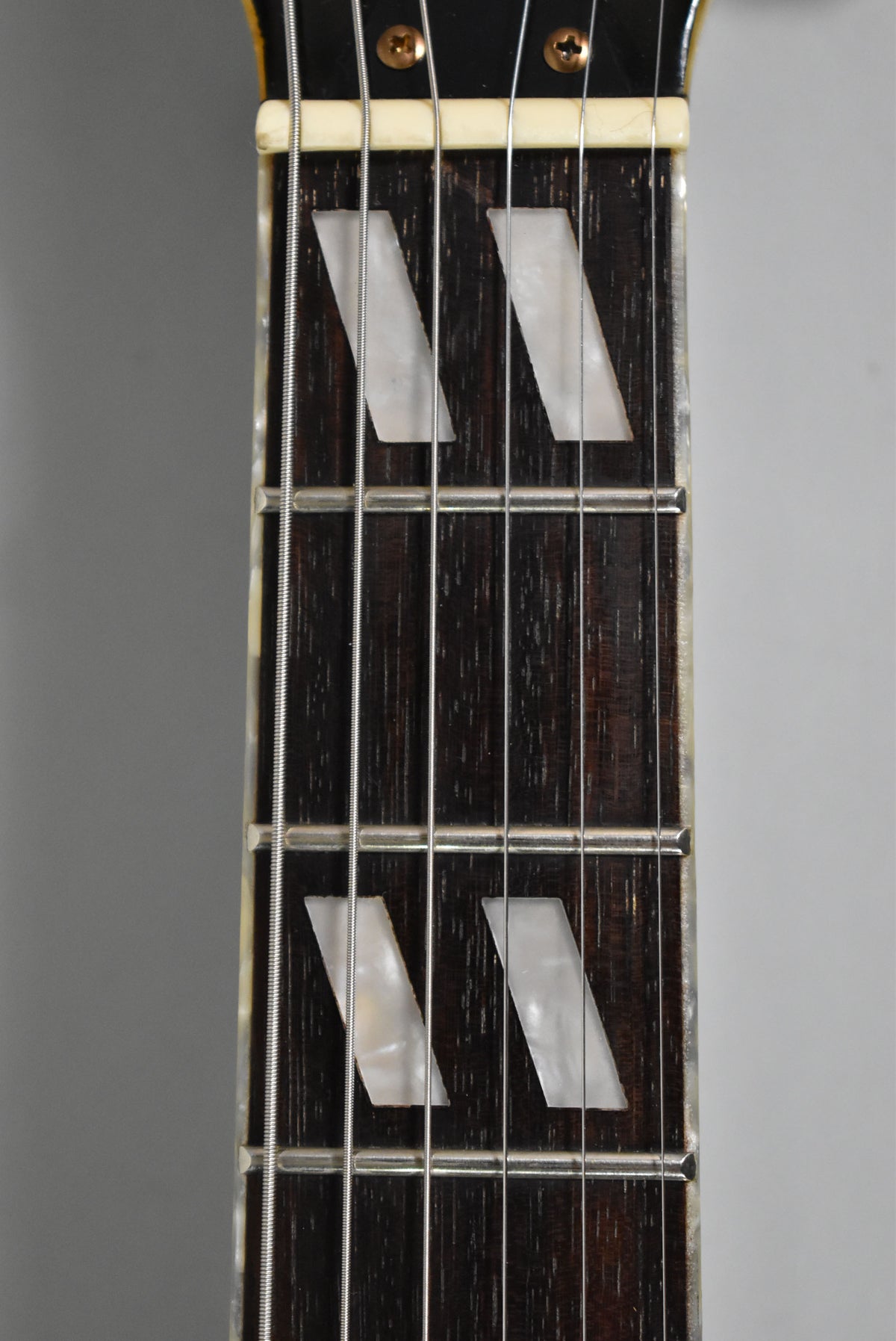 Close-up of the dark rosewood fretboard with trapezoid mother-of-pearl inlays, showing frets 1 through 5 and the bone nut.