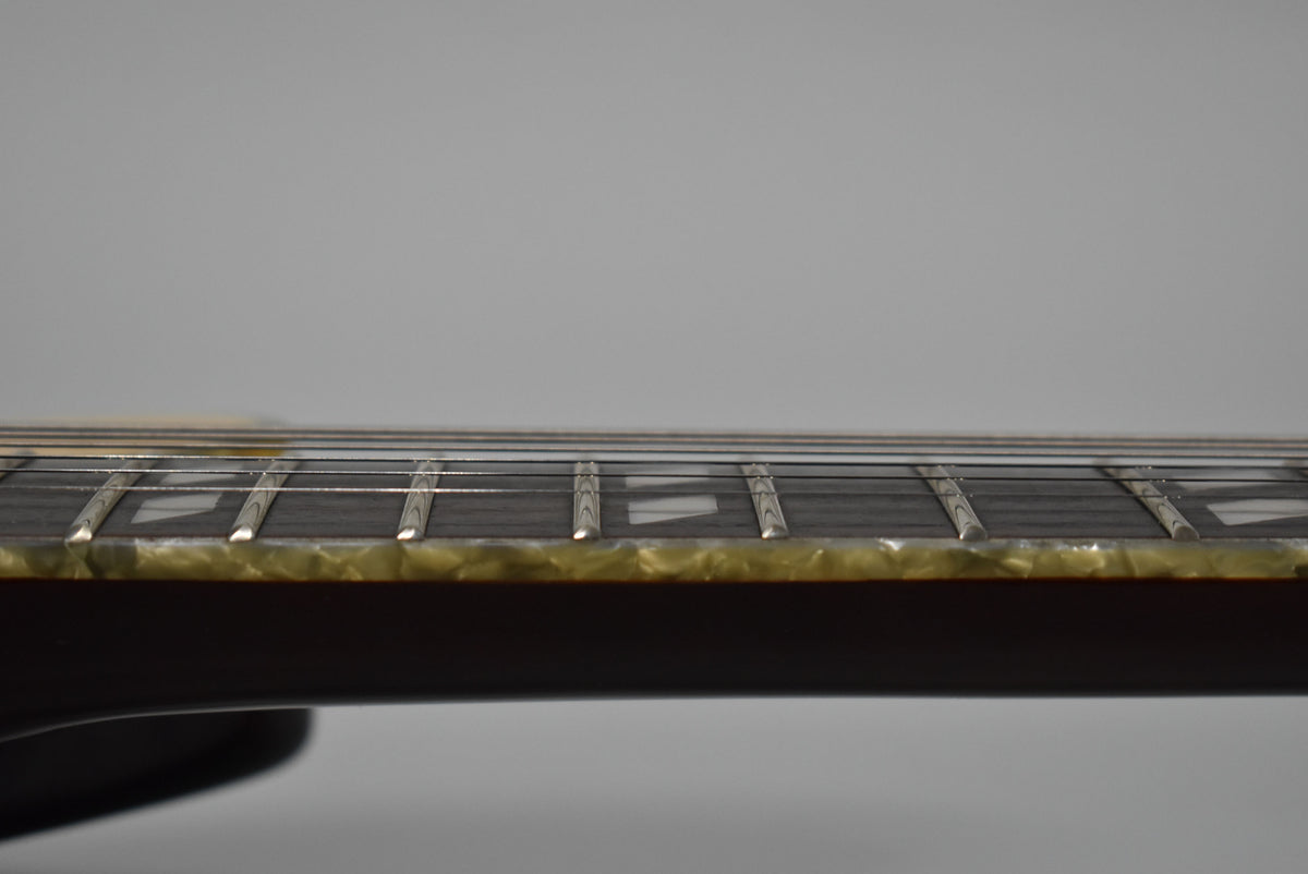 Close-up of the guitar's dark fretboard and frets, showing trapezoid inlays and cream binding with visible wear along the edge.