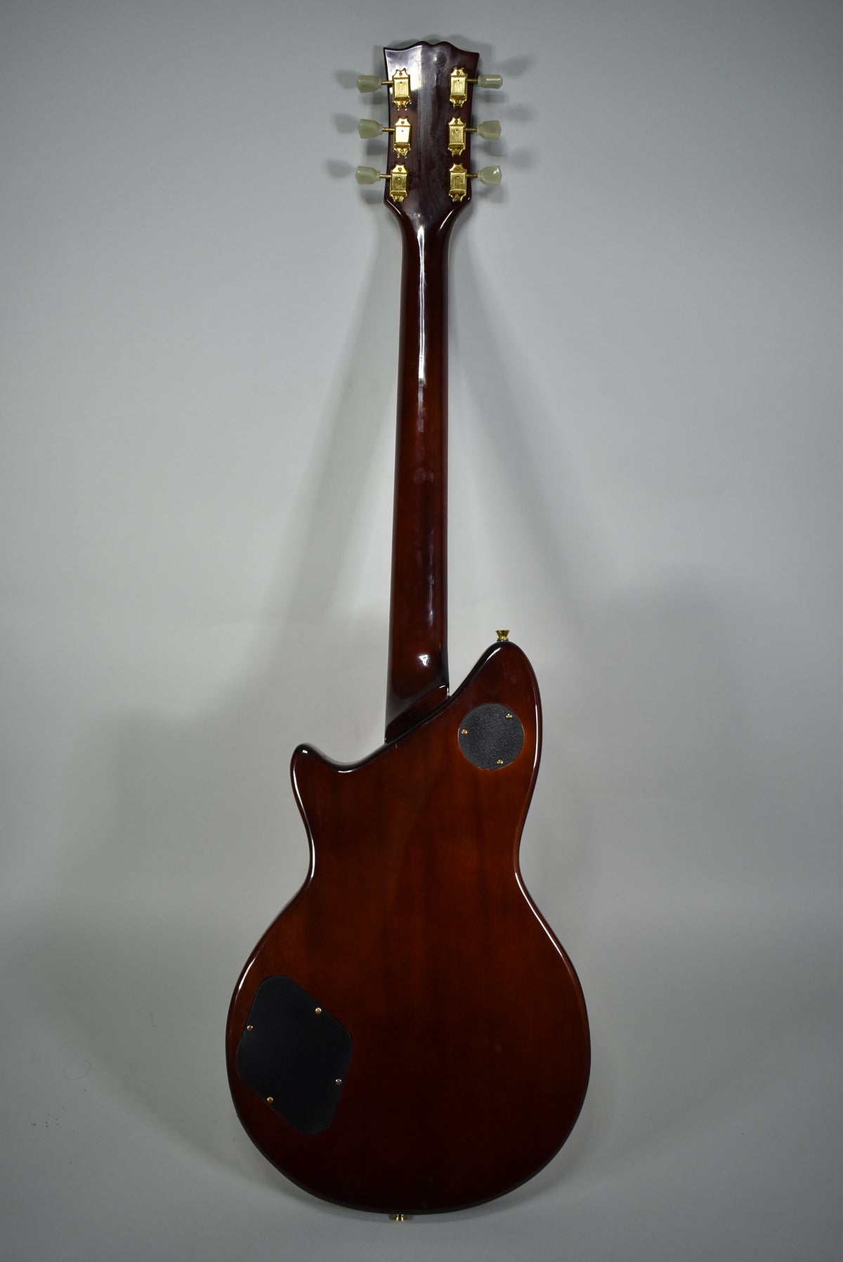Rear view of a natural finish electric guitar with a dark brown body, two black control plates, and gold tuners on the headstock.