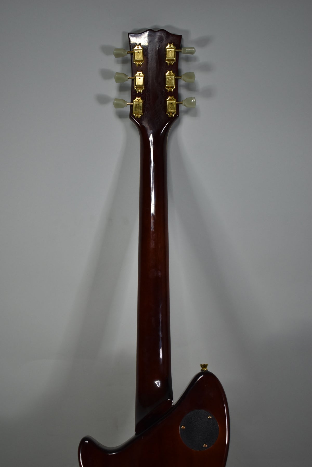 The X3 electric guitar's dark brown neck and headstock are viewed from behind, showing six gold tuners with cream buttons.