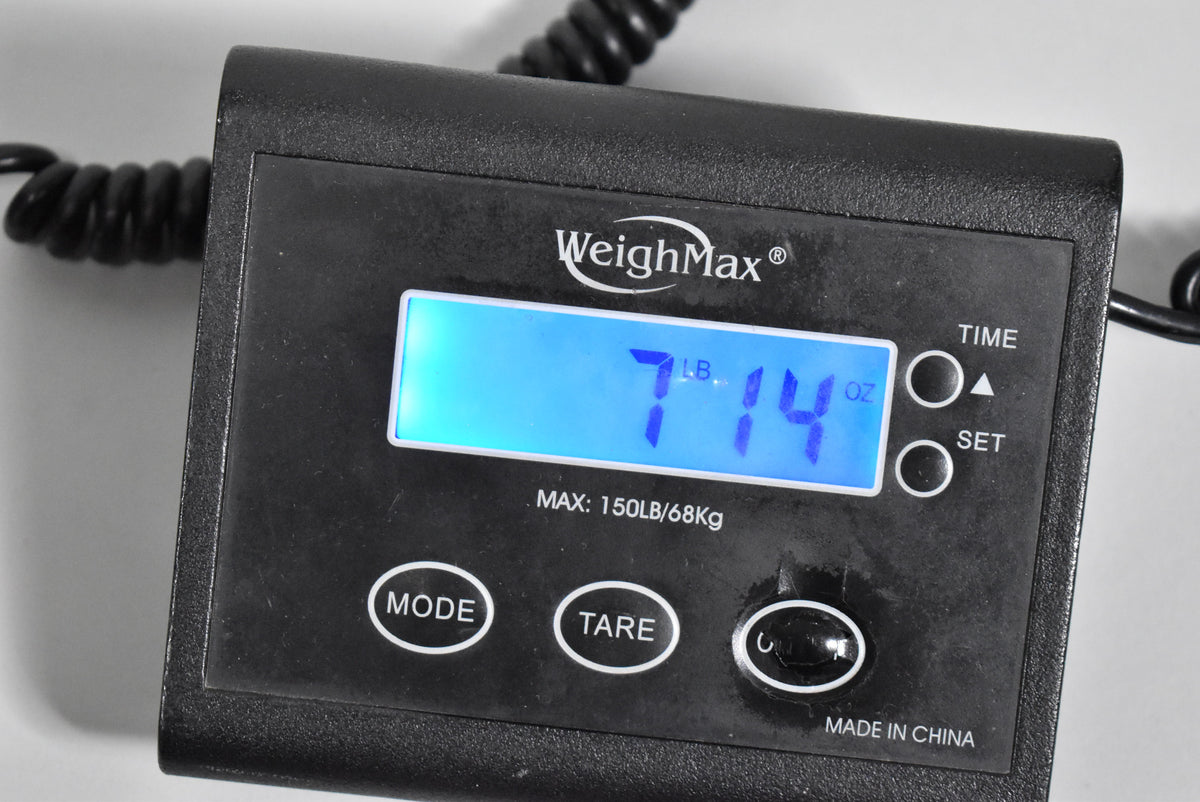 Close-up of a black digital scale displaying "7 LB. 14 OZ." in blue, with "WeighMax" and control buttons visible.