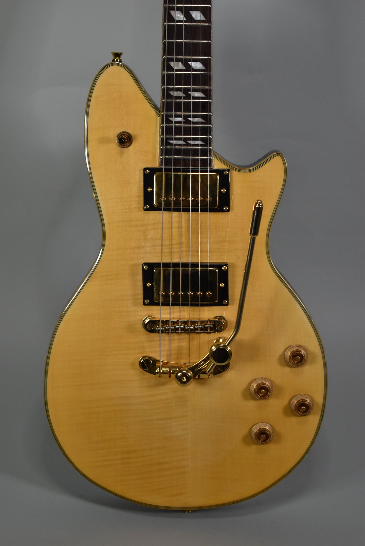The X3 electric guitar, angled slightly, shows its natural flame maple top, gold hardware, two humbuckers, and a Bigsby-style tremolo.