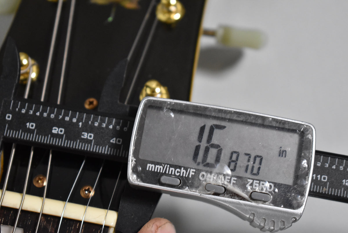 Close-up of the guitar's nut, with a digital caliper measuring its width at 1.6870 inches.