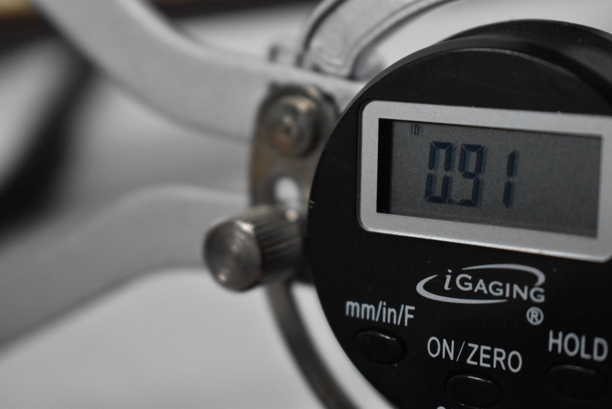 A digital caliper shows a reading of 0.91 inches, with a blurred white object in the background.