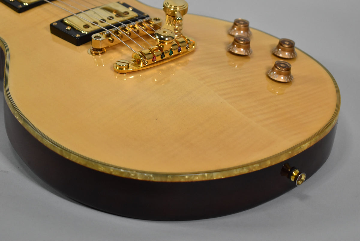 Upper body of a natural finish electric guitar, showing flame maple top, dark mahogany sides, gold hardware, and four amber control knobs.
