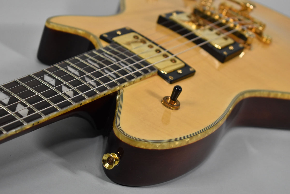 Close-up of the natural finish guitar body, showing the dark fretboard with diamond inlays, gold hardware, and a black toggle switch.