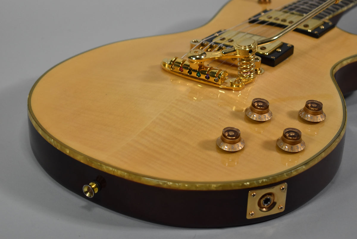 Close-up of the guitar's lower body, showing the natural flame maple top, dark mahogany sides, gold hardware, and four amber control knobs.