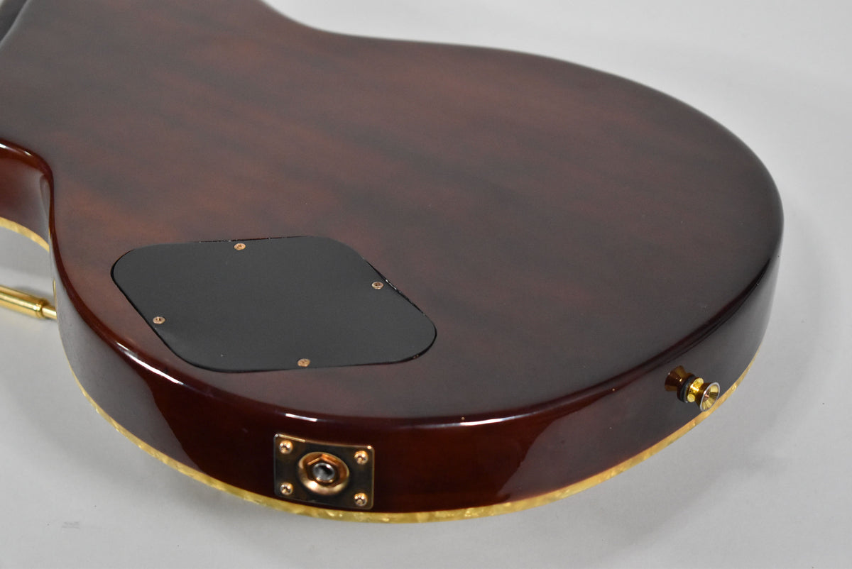 The guitar's dark brown, glossy mahogany back is angled, revealing a black control cavity cover and a gold output jack plate.