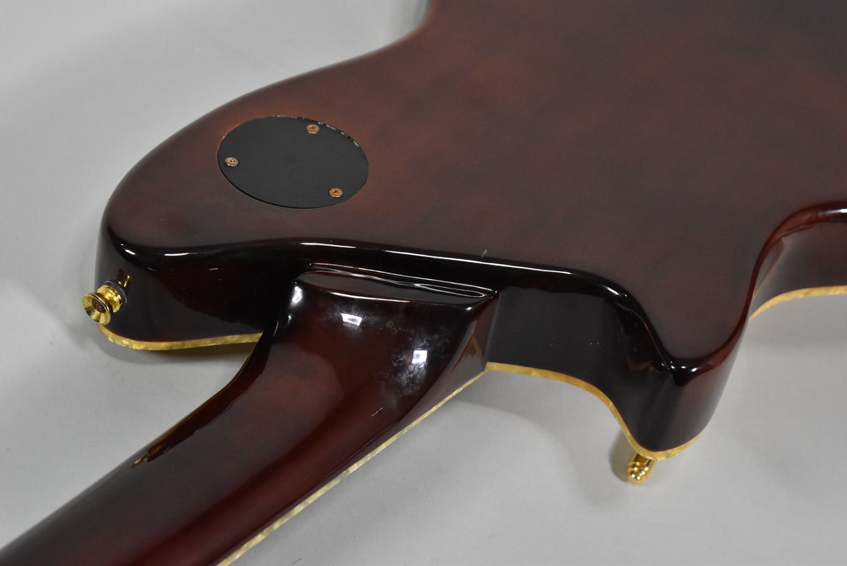 The back of a natural finish electric guitar, showing the dark brown body, neck joint, and gold strap buttons, with some finish wear.
