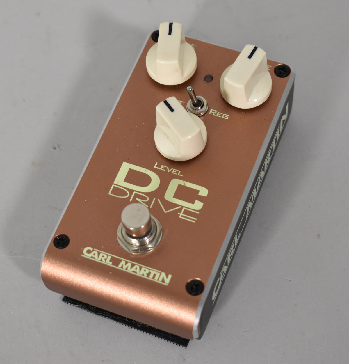 Angled view of a copper-colored pedal with three cream-colored knobs, a small toggle switch, and a silver footswitch.