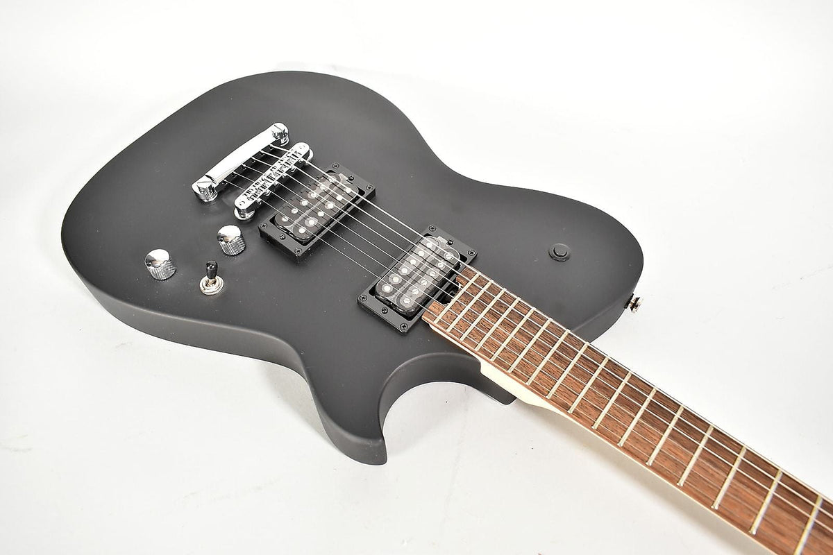 The matte black electric guitar is angled from above, showing its body, two humbuckers, chrome bridge, and part of the fretboard.