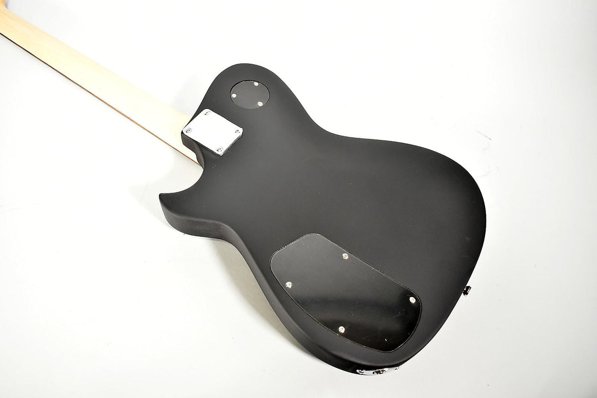 Angled rear view of a matte black electric guitar, showing the light wood neck, neck plate, and two control cavity covers.