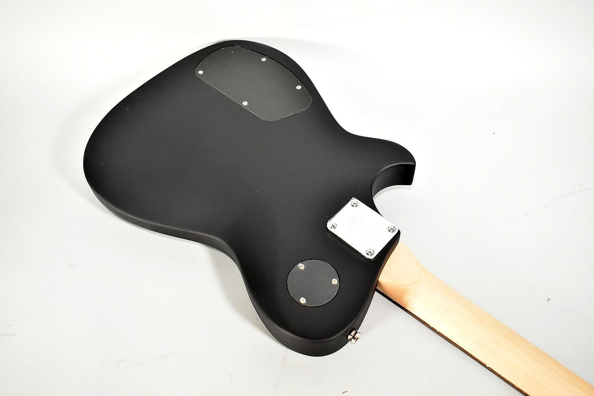 The guitar's matte black body is seen from the back, revealing a light wood neck, chrome neck plate, and two black control covers.