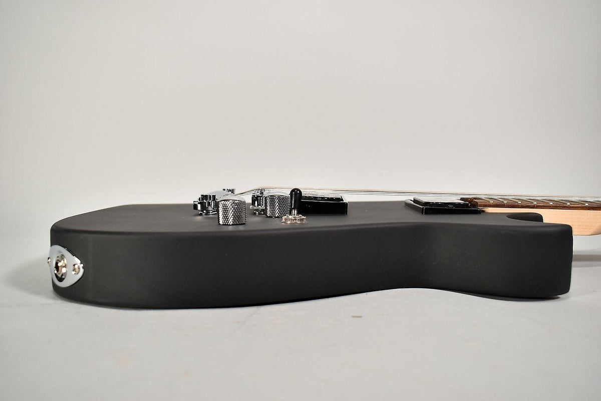The matte black guitar body is viewed from the side, showing the chrome output jack, knurled control knobs, and pickup selector switch.